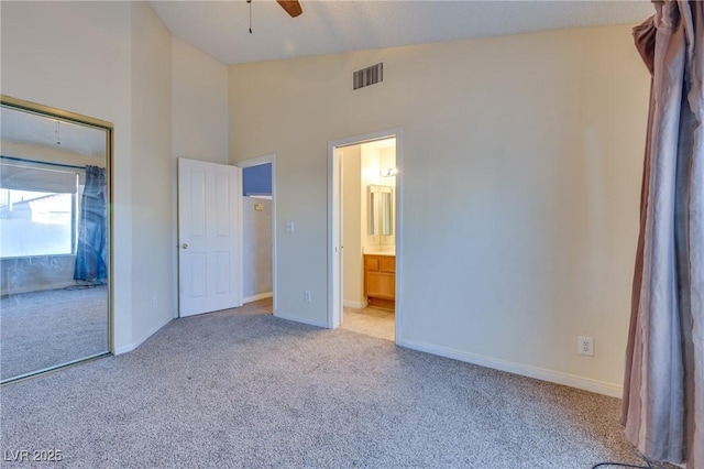 unfurnished bedroom featuring ceiling fan, high vaulted ceiling, ensuite bathroom, light colored carpet, and a closet