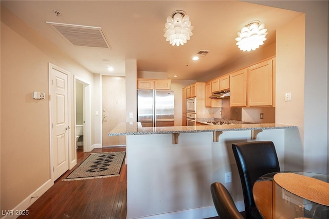 kitchen with light stone countertops, built in appliances, dark hardwood / wood-style floors, kitchen peninsula, and a breakfast bar area