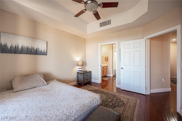 bedroom featuring dark wood-type flooring, ceiling fan, connected bathroom, and a raised ceiling