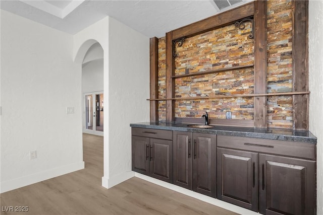 bar featuring dark brown cabinetry, sink, and dark wood-type flooring