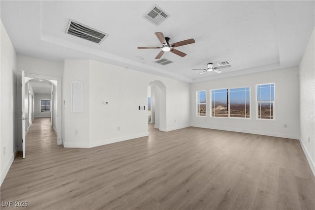 unfurnished living room with a raised ceiling, ceiling fan, and light wood-type flooring