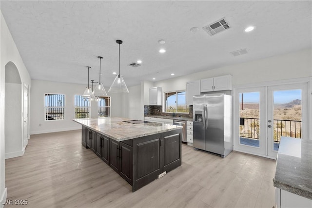 kitchen featuring pendant lighting, appliances with stainless steel finishes, white cabinetry, backsplash, and a kitchen island