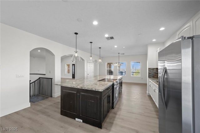 kitchen featuring appliances with stainless steel finishes, pendant lighting, white cabinetry, a kitchen island with sink, and light hardwood / wood-style floors