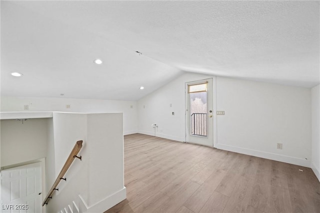 additional living space with lofted ceiling, light hardwood / wood-style flooring, and a textured ceiling