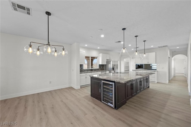 kitchen with stainless steel refrigerator with ice dispenser, a center island, white cabinets, and decorative light fixtures