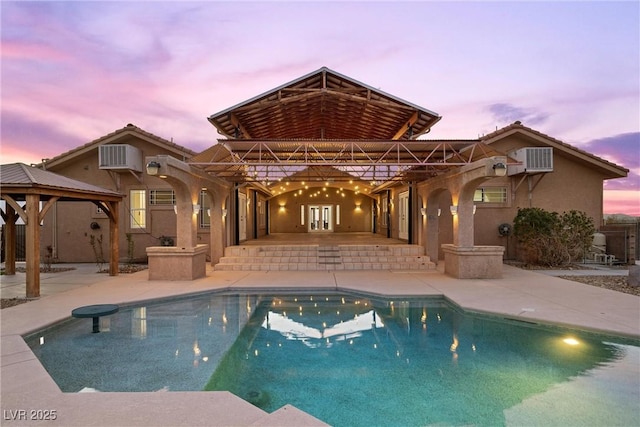 pool at dusk with a gazebo, a patio, and a wall mounted AC