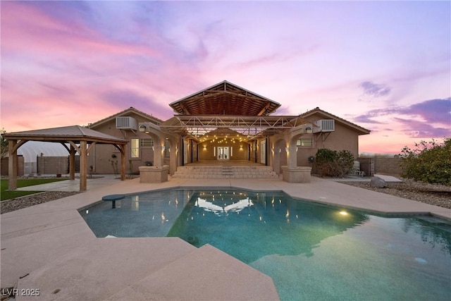 pool at dusk with a gazebo, a wall mounted AC, and a patio