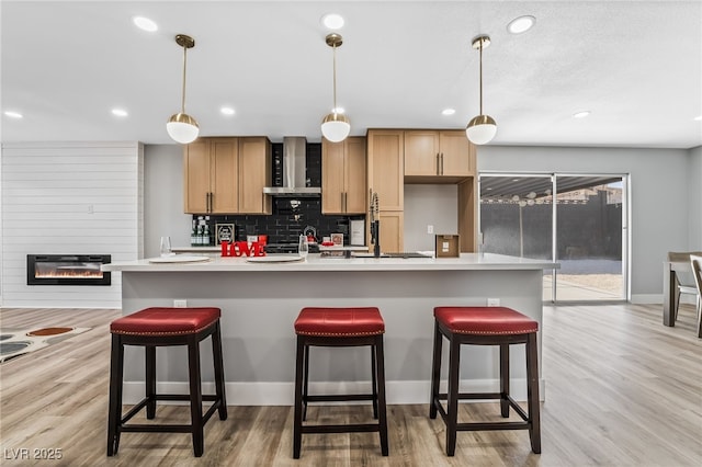 kitchen featuring an island with sink, a large fireplace, wall chimney range hood, pendant lighting, and a breakfast bar