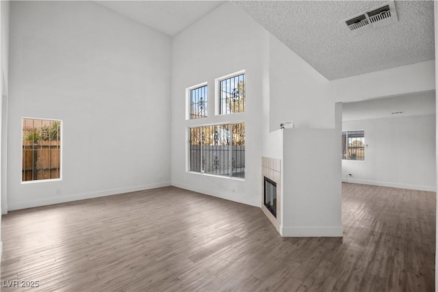 unfurnished living room featuring high vaulted ceiling, hardwood / wood-style floors, and a tile fireplace