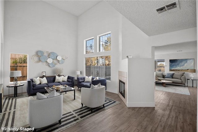 living room with hardwood / wood-style flooring, a textured ceiling, a high ceiling, and a tile fireplace