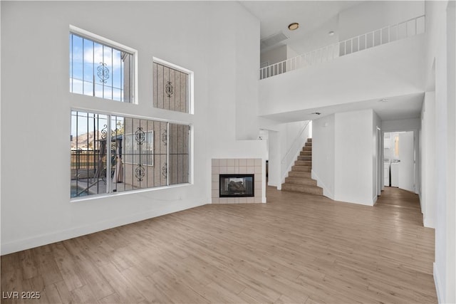 unfurnished living room featuring a towering ceiling, light hardwood / wood-style flooring, and a tile fireplace