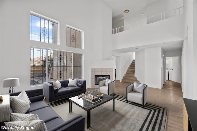 living room with a high ceiling, light hardwood / wood-style flooring, and a tiled fireplace