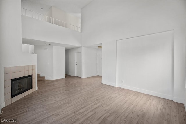 unfurnished living room with a high ceiling, a tiled fireplace, and light wood-type flooring