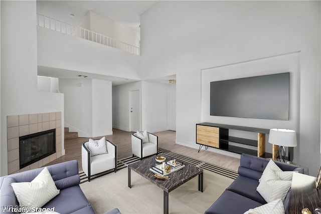 living room featuring light wood-type flooring, a towering ceiling, and a tile fireplace