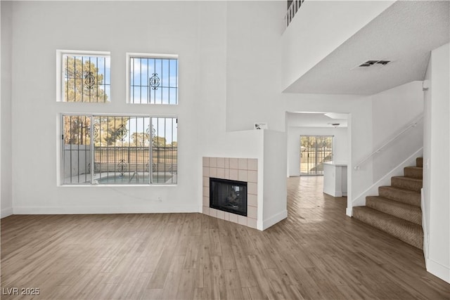 unfurnished living room featuring a high ceiling, hardwood / wood-style floors, and a tile fireplace