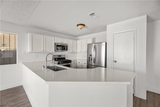 kitchen featuring white cabinetry, hardwood / wood-style floors, kitchen peninsula, stainless steel appliances, and sink