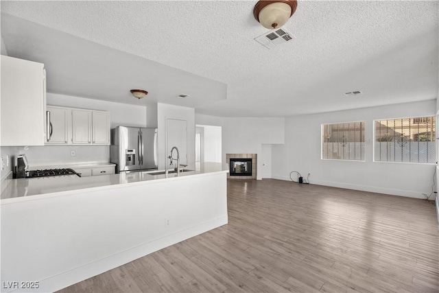 kitchen featuring white cabinetry, kitchen peninsula, stainless steel refrigerator with ice dispenser, a fireplace, and sink