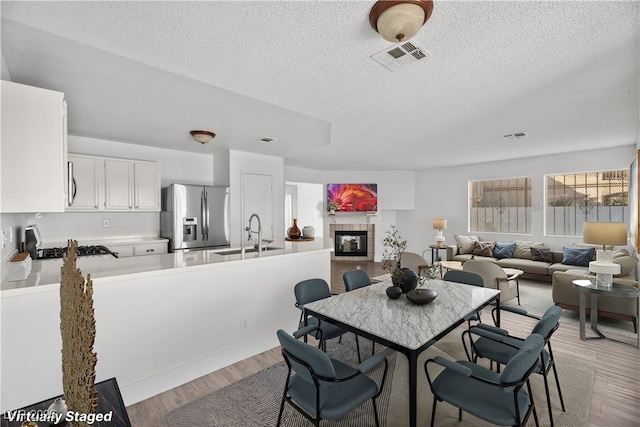 dining area with a textured ceiling, light hardwood / wood-style flooring, a tile fireplace, and sink