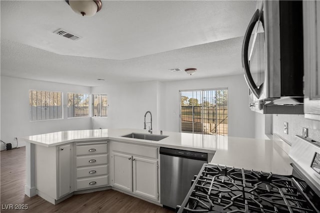 kitchen with kitchen peninsula, appliances with stainless steel finishes, a textured ceiling, white cabinets, and sink