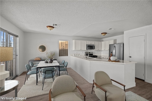 kitchen with white cabinetry, kitchen peninsula, stainless steel appliances, wood-type flooring, and a textured ceiling