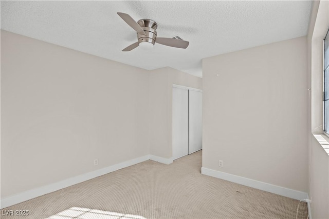 empty room with ceiling fan, light colored carpet, and a textured ceiling