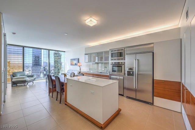 kitchen featuring light tile patterned flooring, a center island, built in appliances, and a wall of windows