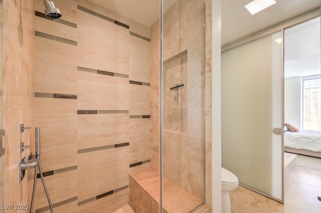 bathroom with toilet, a tile shower, and tile patterned flooring