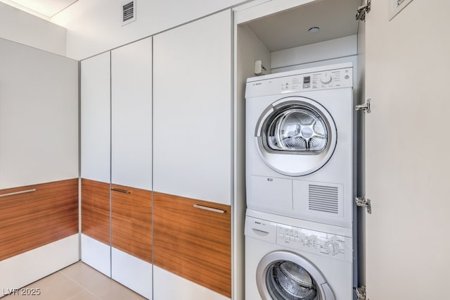 laundry area with light tile patterned floors and stacked washer / dryer