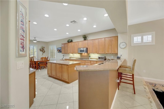 kitchen with a kitchen bar, black gas cooktop, kitchen peninsula, ceiling fan, and light tile patterned floors