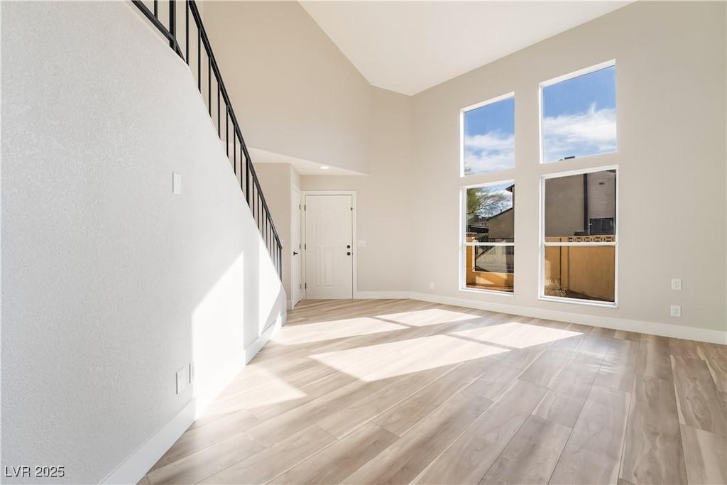 unfurnished living room with light wood-type flooring and a towering ceiling