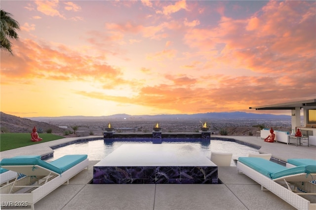 pool at dusk with a mountain view, pool water feature, and a patio