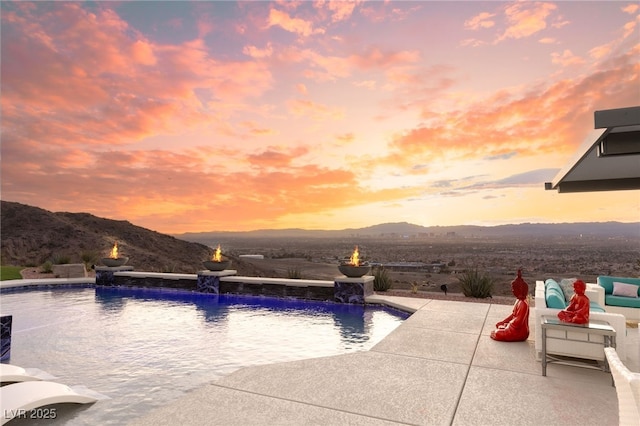 pool at dusk featuring pool water feature, a mountain view, and a patio area