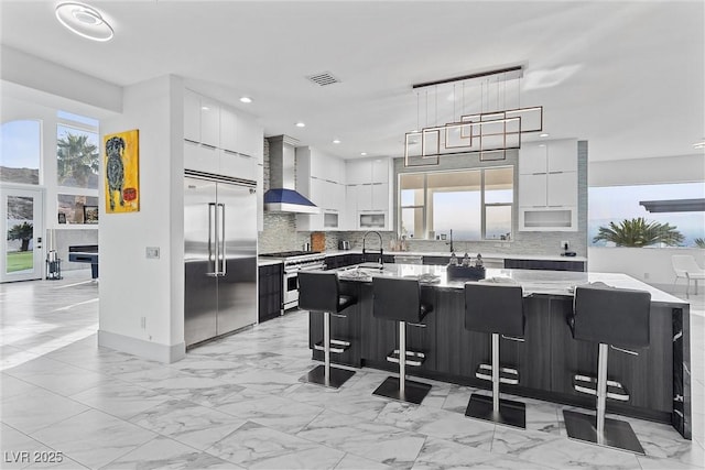 kitchen featuring a kitchen island, wall chimney exhaust hood, high quality appliances, and a breakfast bar