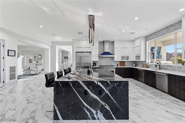 kitchen featuring white cabinets, wall chimney range hood, a large island, a breakfast bar, and high quality appliances