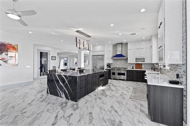 kitchen featuring white cabinets, premium appliances, decorative backsplash, a large island, and wall chimney range hood