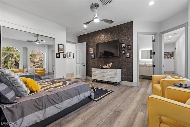 bedroom featuring ceiling fan, ensuite bathroom, a closet, and light hardwood / wood-style floors