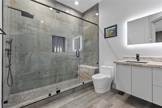 bathroom featuring a shower with door, vanity, hardwood / wood-style floors, and toilet