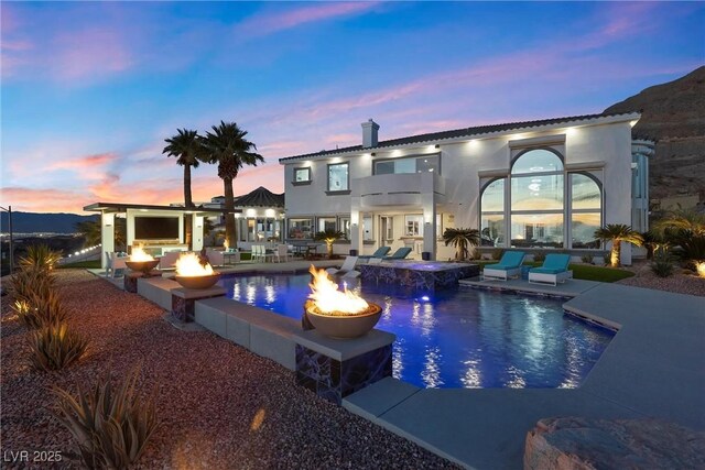 pool at dusk with a patio area and a fire pit