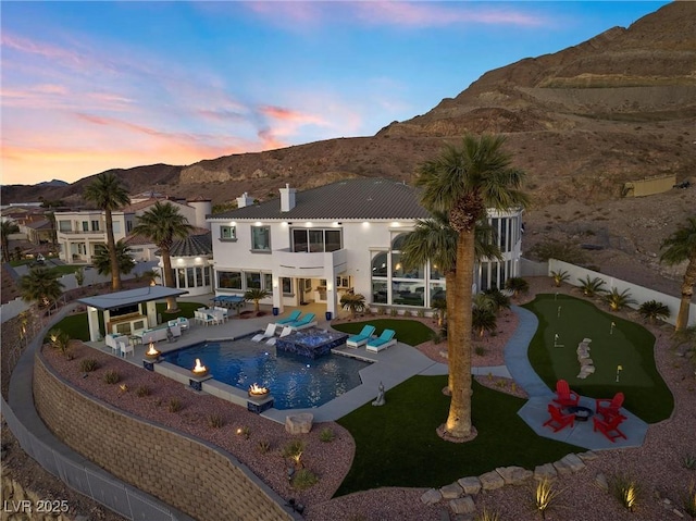 pool at dusk with a hot tub, outdoor lounge area, a mountain view, and a patio