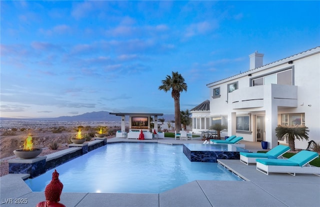 pool at dusk with an outdoor fire pit, a mountain view, and a patio