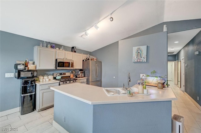 kitchen featuring vaulted ceiling, appliances with stainless steel finishes, rail lighting, light tile patterned floors, and kitchen peninsula