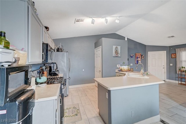 kitchen with appliances with stainless steel finishes, lofted ceiling, sink, track lighting, and a center island with sink