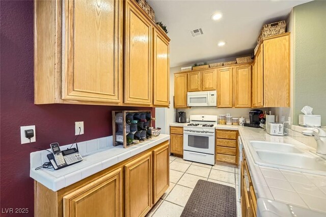 kitchen with sink, white appliances, light tile patterned floors, and tile counters