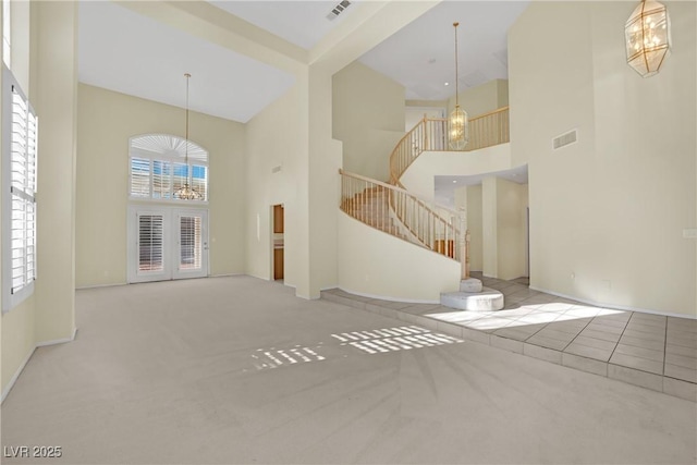 unfurnished living room featuring a notable chandelier, light colored carpet, and a high ceiling