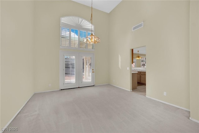 carpeted empty room featuring french doors, a towering ceiling, and an inviting chandelier