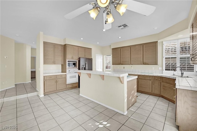 kitchen with sink, stainless steel appliances, a kitchen breakfast bar, tile counters, and a kitchen island