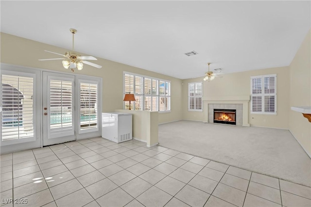 unfurnished living room with ceiling fan, a fireplace, light colored carpet, and a wealth of natural light