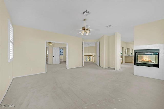 unfurnished living room with a multi sided fireplace, light carpet, and ceiling fan