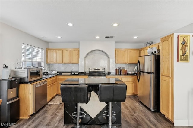 kitchen with a kitchen bar, light brown cabinetry, appliances with stainless steel finishes, and a kitchen island