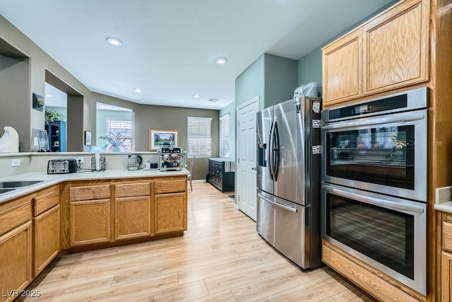 kitchen featuring kitchen peninsula, appliances with stainless steel finishes, sink, and light hardwood / wood-style flooring